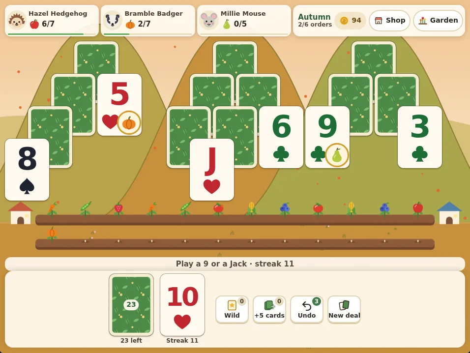 Actual Cozy Peaks Solitaire gameplay in autumn: three peaks of cards on olive and golden hills, with face-up cards including a 5 of hearts with a pumpkin sticker and a 9 of clubs with a pear sticker. The waste card is the 10 of hearts with a streak of 11, the stock holds 23 cards, and three orders at the top ask for apples, pumpkins and pears. Below the peaks the garden bed shows thirteen crop plants for the orders filled so far.