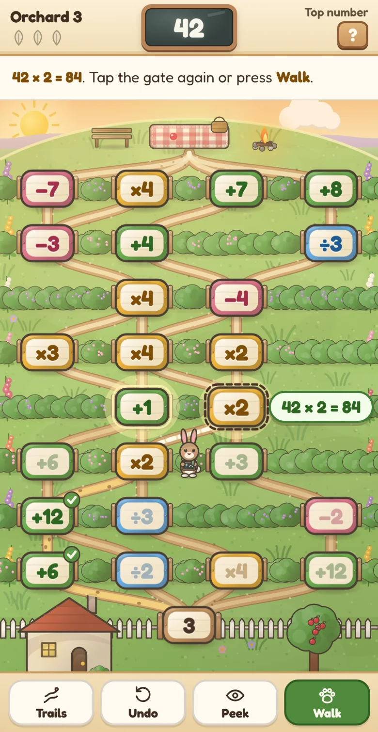Actual Hollyhock Math Path gameplay on a phone held upright: a hillside of hedgerow gardens with painted gate signs in green, rose, honey gold and sky blue, Tally the rabbit partway up the hill with 42 on the slate, the two gates she can reach next glowing, the chosen ×2 gate with its sum, 42 × 2 = 84, in a bubble beside it, and the Trails, Undo, Peek and Walk buttons in a row along the bottom.